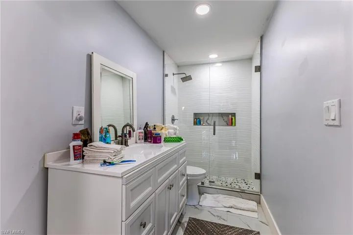 Bathroom featuring toilet, vanity, baseboards, marble finish floor, and a shower stall