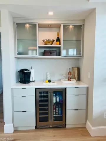Indoor dry bar with modern cabinets, wine cooler, and light wood-style flooring