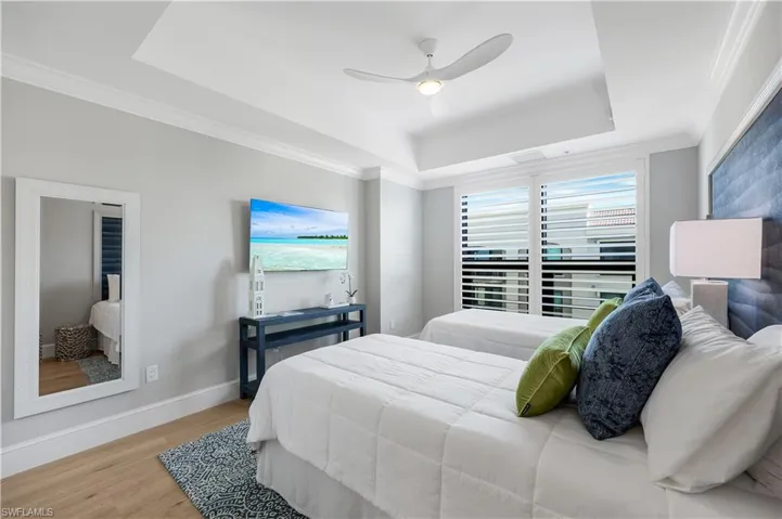 Guest Bedroom featuring a tray ceiling, wood finished floors, ornamental molding, a ceiling fan and a wall TV