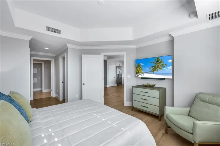 Primary Bedroom featuring ornamental molding, light wood floors ,a tray ceiling and a wall mount TV.