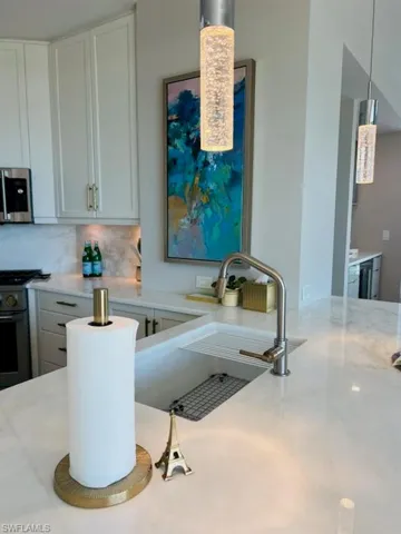 Kitchen featuring decorative backsplash, white cabinetry, appliances with stainless steel finishes, light stone counters, and hanging light fixtures
