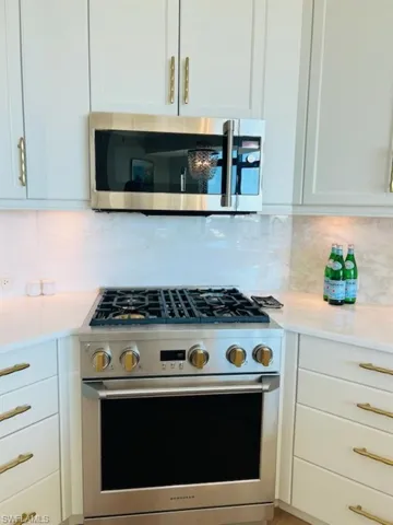 Kitchen featuring stainless steel appliances, white cabinetry, light stone countertops, and backsplash