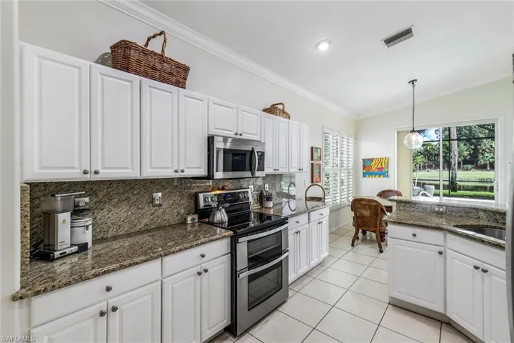 Kitchen featuring white cabinets, stainless steel appliances, decorative light fixtures, and dark stone counters