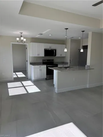 Kitchen featuring decorative light fixtures, stainless steel electric range oven, white cabinetry, a chandelier, and light stone counters