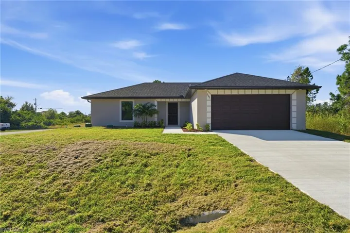 Ranch-style home with driveway, a front yard, a garage, stucco siding, and roof with shingles