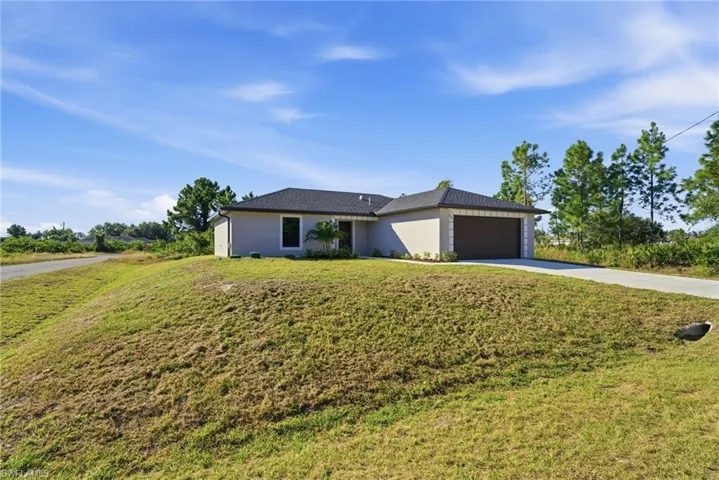 View of front of property featuring driveway, a front lawn, stucco siding, and an attached garage
