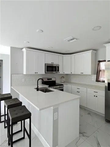 Kitchen with tasteful backsplash, stainless steel appliances, white cabinetry, light marble finish flooring, and a kitchen bar