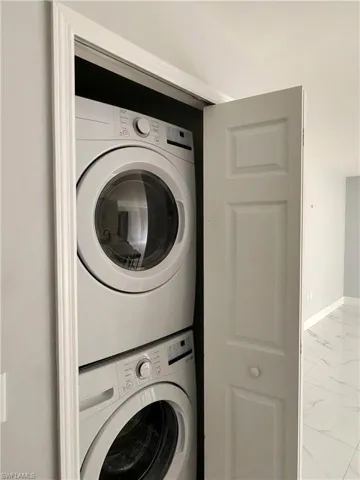 Laundry area featuring light marble finish floors and stacked washer / dryer