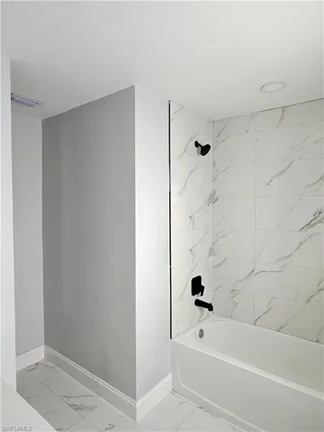 Full bathroom with shower / tub combination and light marble finish floors