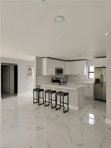 Kitchen featuring stainless steel appliances, white cabinets, tasteful backsplash, a kitchen bar, and a peninsula
