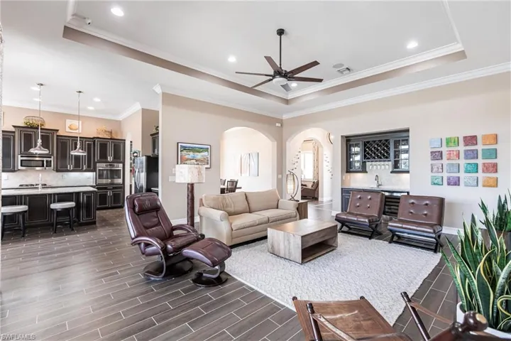 Living area with arched walkways, a raised ceiling, crown molding, wood finish floors, and recessed lighting