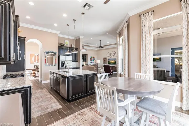Kitchen featuring a ceiling fan, light stone counters, wood finish floors, crown molding, and arched walkways
