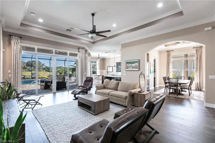 Living area with a tray ceiling, plenty of natural light, ceiling fan, dark wood-style flooring, and crown molding