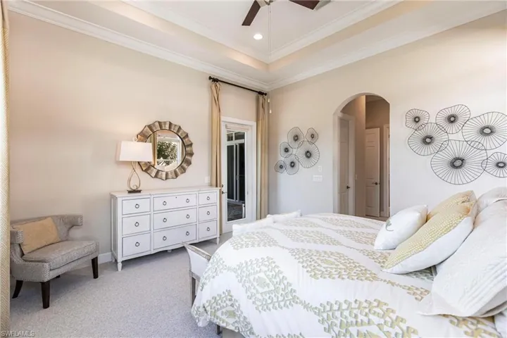 Bedroom with arched walkways, ornamental molding, carpet flooring, a raised ceiling, and a ceiling fan