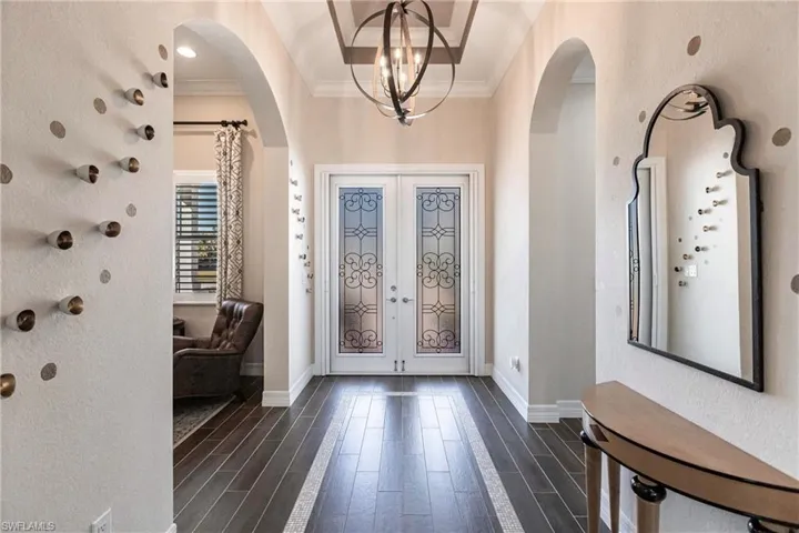 Foyer with a textured wall, wood tiled floors, a chandelier, ornamental molding, and french doors