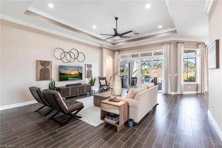 Living area with a tray ceiling, ornamental molding, arched walkways, dark wood-style flooring, and recessed lighting