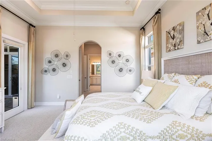 Carpeted bedroom with arched walkways, ensuite bathroom, ornamental molding, a raised ceiling, and access to exterior