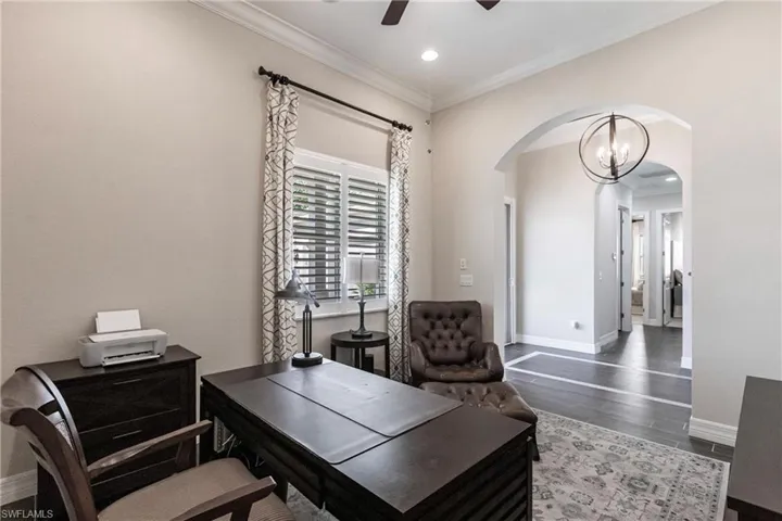 Office area featuring a chandelier, ornamental molding, arched walkways, dark wood-type flooring, and ceiling fan