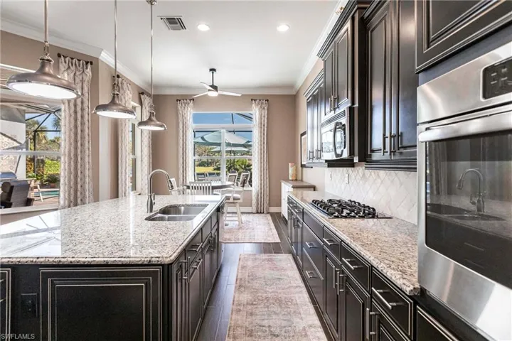 Kitchen featuring appliances with stainless steel finishes, crown molding, light stone countertops, dark wood-style flooring, and dark cabinets