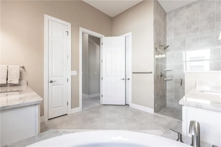 Full bath featuring vanity, a stall shower, light tile patterned flooring, and a tub to relax in