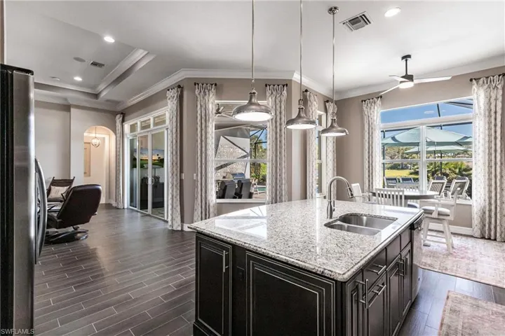 Kitchen featuring ornamental molding, recessed lighting, dark cabinets, plenty of natural light, and light stone counters