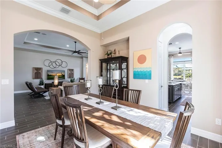 Dining space with a tray ceiling, arched walkways, a ceiling fan, wood tiled floors, and crown molding
