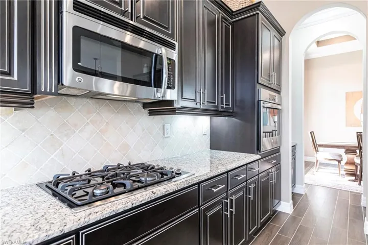 Kitchen featuring light stone counters, stainless steel appliances, backsplash, wood tiled floors, and crown molding