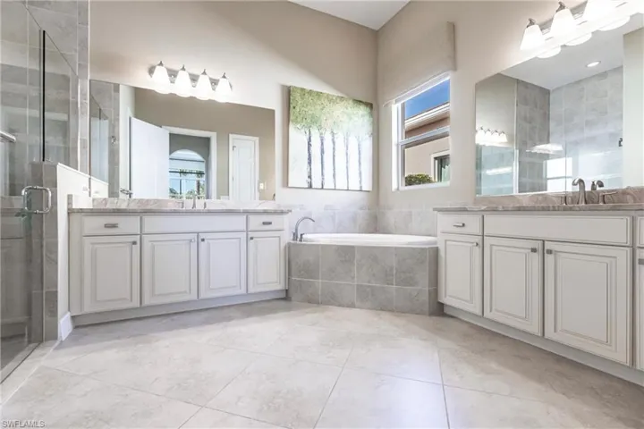 Bathroom with a stall shower, light tile patterned floors, two vanities, and a bath