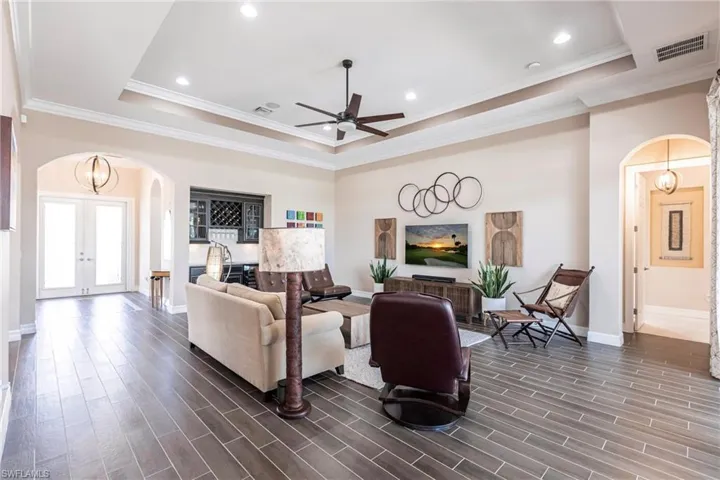 Living area featuring arched walkways, a raised ceiling, a chandelier, wood finish floors, and crown molding