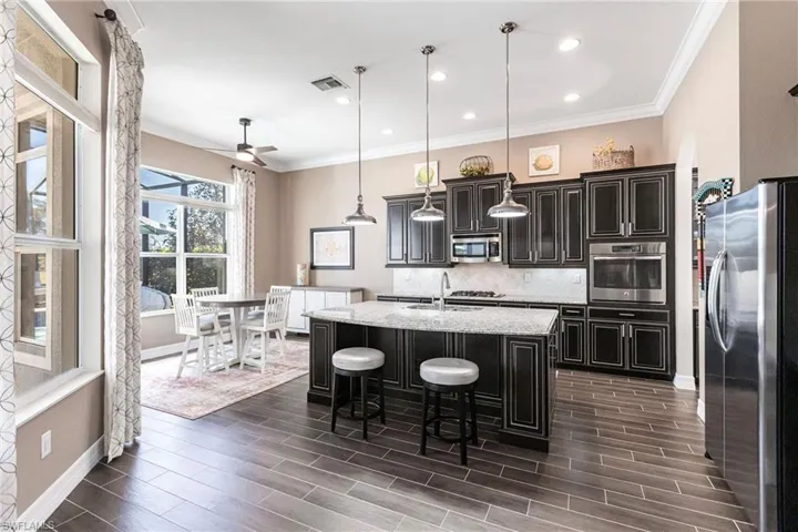 Kitchen featuring hanging light fixtures, ornamental molding, decorative backsplash, stainless steel appliances, and dark cabinets