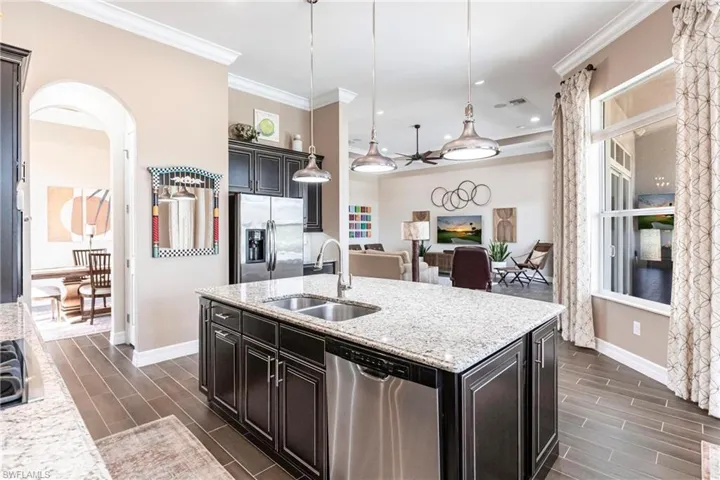 Kitchen featuring arched walkways, wood tiled floors, a center island with sink, stainless steel appliances, and crown molding