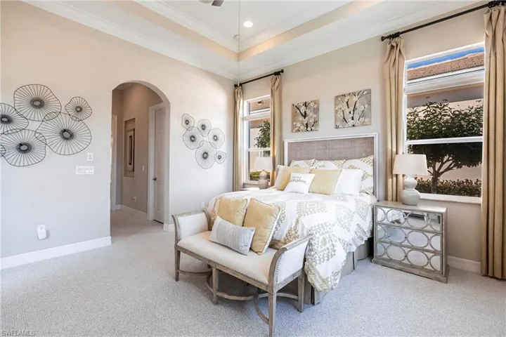 Bedroom featuring arched walkways, light colored carpet, ornamental molding, a tray ceiling, and ceiling fan
