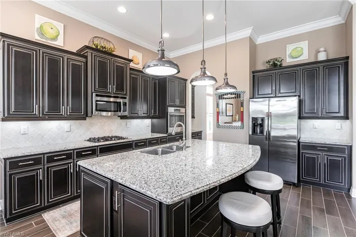 Kitchen featuring backsplash, wood tiled floors, appliances with stainless steel finishes, pendant lighting, and ornamental molding