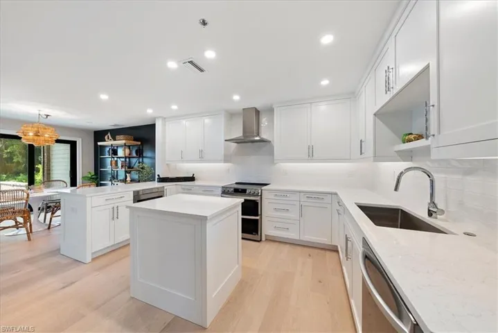 Kitchen with sink, light hardwood / wood-style flooring, appliances with stainless steel finishes, and wall chimney exhaust hood