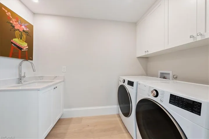 Laundry area featuring sink, cabinets, washer and dryer, and light hardwood / wood-style floors