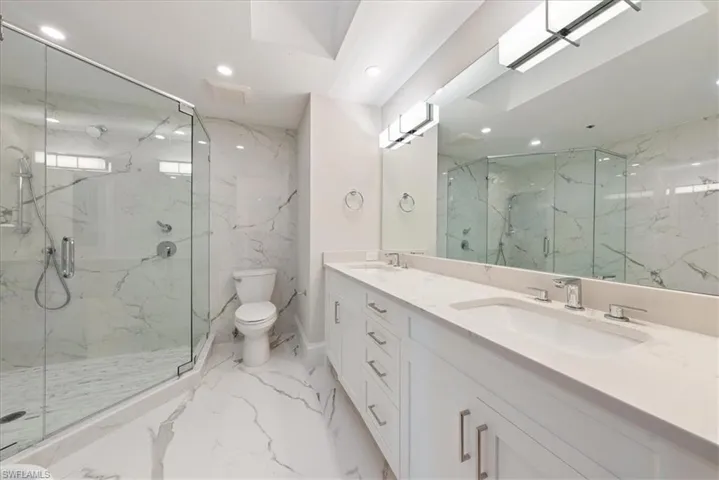 Bathroom featuring walk in shower, tile patterned floors, toilet, and dual bowl vanity