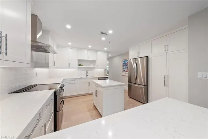 Kitchen featuring appliances with stainless steel finishes, light hardwood / wood-style flooring, decorative backsplash, light stone countertops, and wall chimney exhaust hood