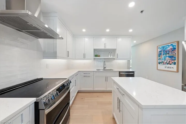 Kitchen with tasteful backsplash, wall chimney range hood, sink, light hardwood / wood-style floors, and appliances with stainless steel finishes