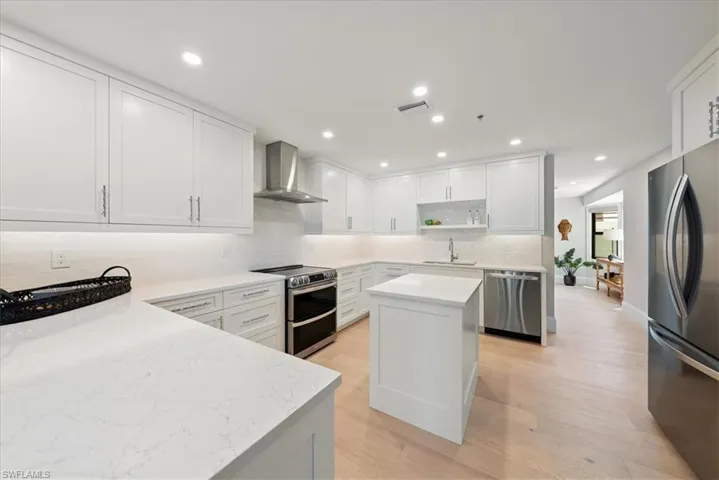 Kitchen with light hardwood / wood-style floors, appliances with stainless steel finishes, wall chimney exhaust hood, and a kitchen island