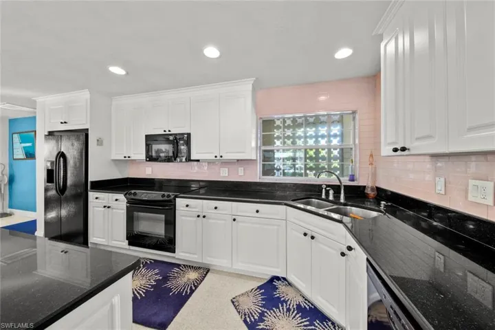 Kitchen featuring backsplash, sink, white cabinets, and black appliances