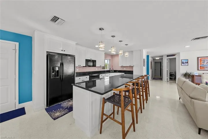Kitchen featuring black appliances, white cabinets, hanging light fixtures, a kitchen island, and a kitchen bar