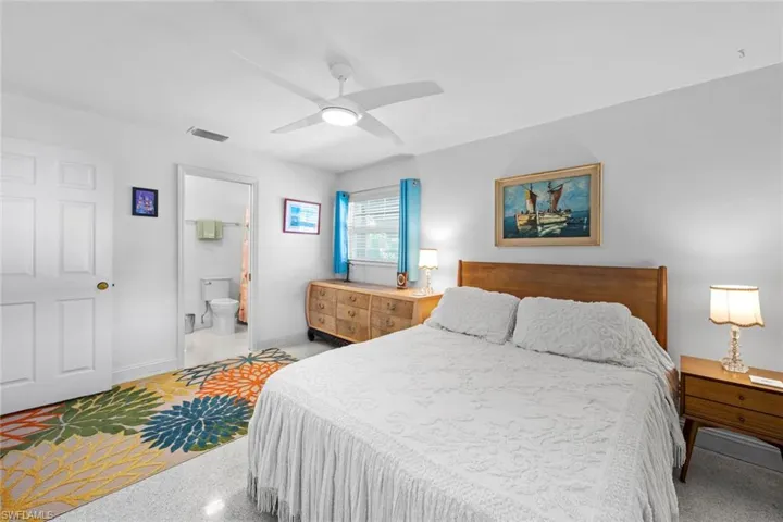 Bedroom with ceiling fan, light colored carpet, and ensuite bath