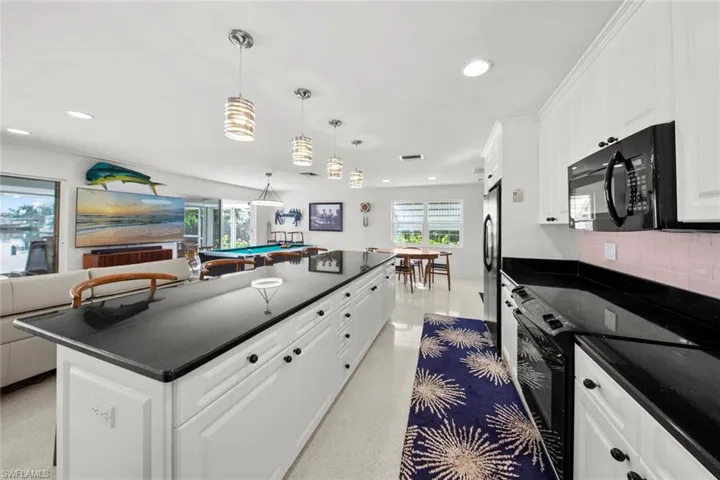 Kitchen with tasteful backsplash, black appliances, pendant lighting, white cabinets, and pool table