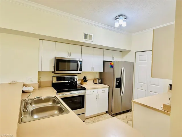 Kitchen with appliances with stainless steel finishes, ornamental molding, light countertops, a textured ceiling, and light tile patterned floors