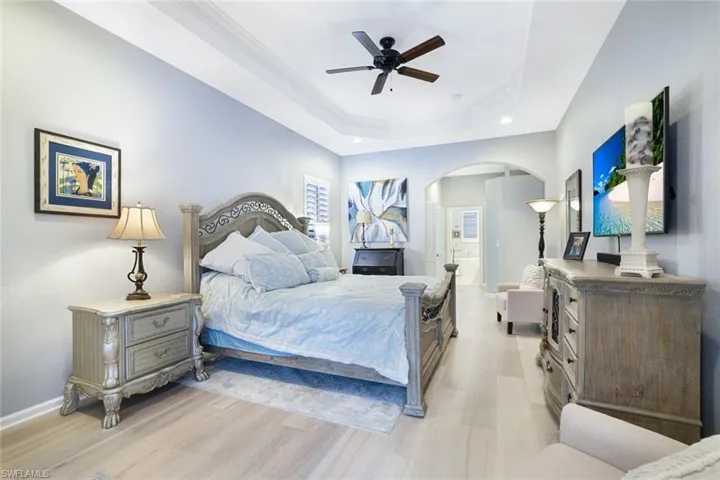 Bedroom with a tray ceiling, ornamental molding, light hardwood / wood-style flooring, and ceiling fan