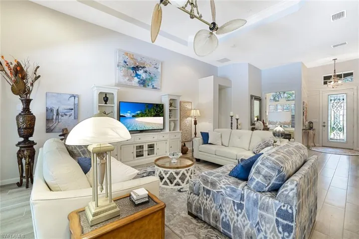 Living room featuring light hardwood / wood-style flooring, ceiling fan, ornamental molding, and a tray ceiling