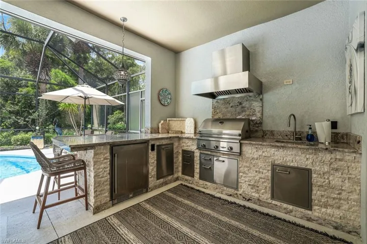 Kitchen featuring a breakfast bar area, decorative light fixtures, fridge, plenty of natural light, and wall chimney range hood