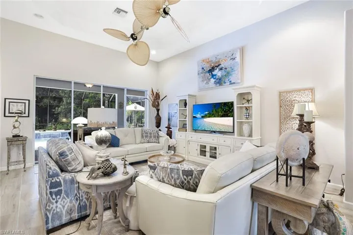 Living room featuring light hardwood / wood-style flooring, ceiling fan, a raised ceiling, and a high ceiling