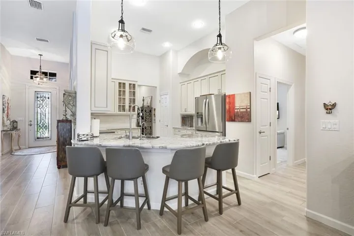 Kitchen with light wood-type flooring, stainless steel fridge, decorative light fixtures, and sink