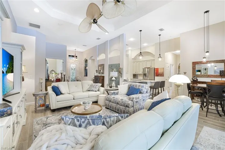 Living room with crown molding, ceiling fan, light wood-type flooring, and a tray ceiling
